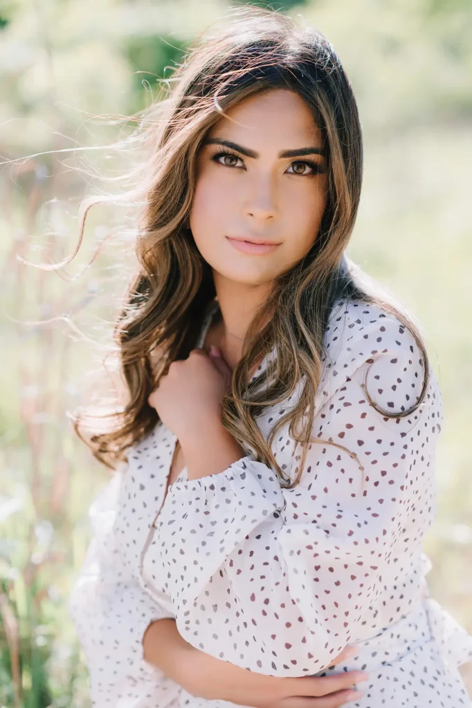 Portrait of high school senior with soft glam makeup and wavy curls in a field